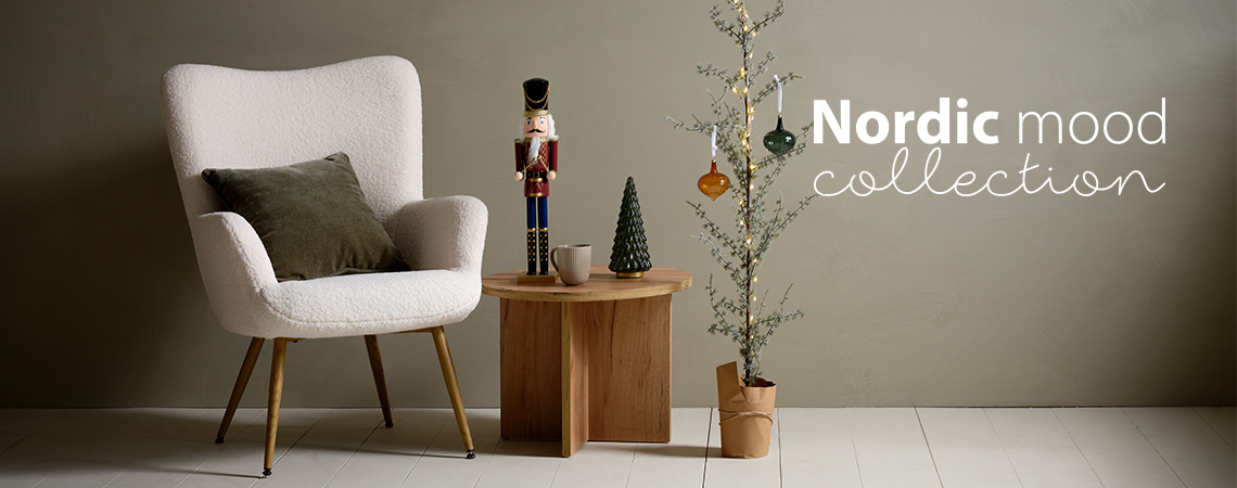 Poltrona com almofada, mesa de apoio com figura natalícia e uma pequena árvore de natal decorada com enfeites de vidro