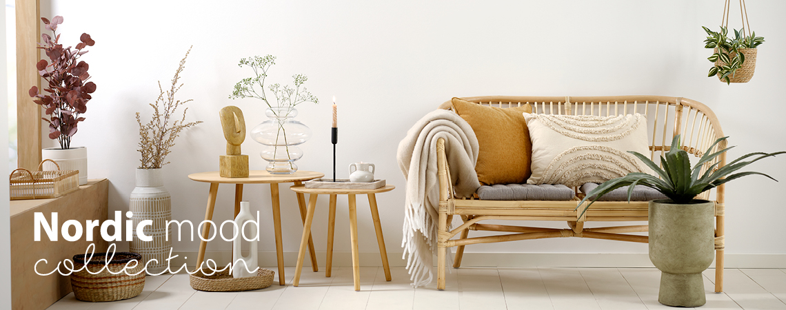 Mesas de apoio com jarra de vidro, castiçal e escultura, vaso e planta artificial, sofá de rattan com almofadas e manta