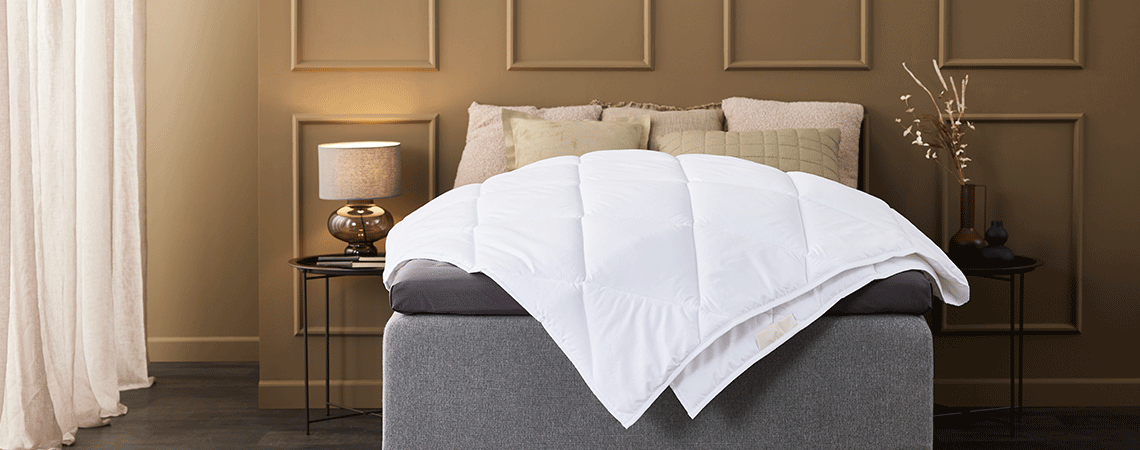 Quarto castanho claro com cama com almofadas decorativas, edredões e colchão superior