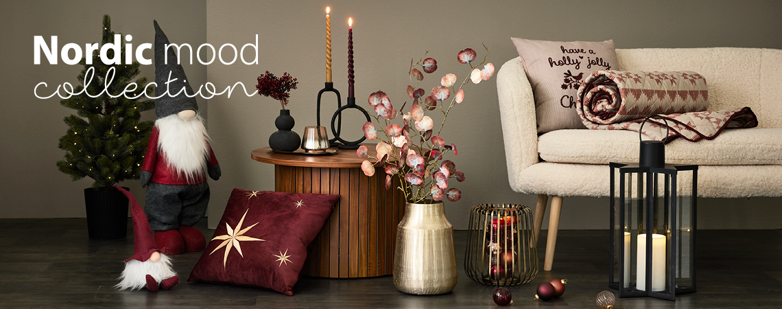 Elfos de Natal, almofadas, vaso dourado com flor artificial, candelabro dourado e lanterna preta em frente de um sofá branco