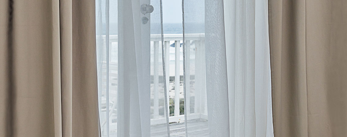 Vista para uma varanda através de uma porta aberta com cortinas esvoaçantes