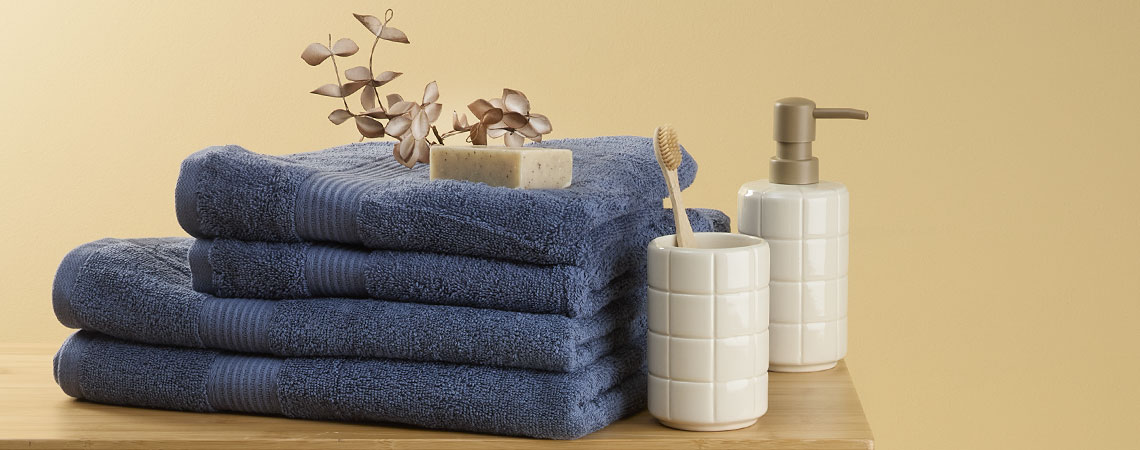Pilha de toalhas azuis num banco com um suporte para escovas de dentes e um dispensador de sabão 