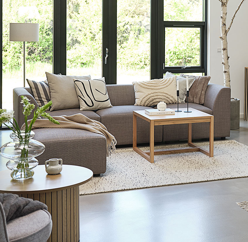 Mesa de centro minimalista em carvalho numa sala de estar luminosa com um sofá grande e almofadas decorativas 