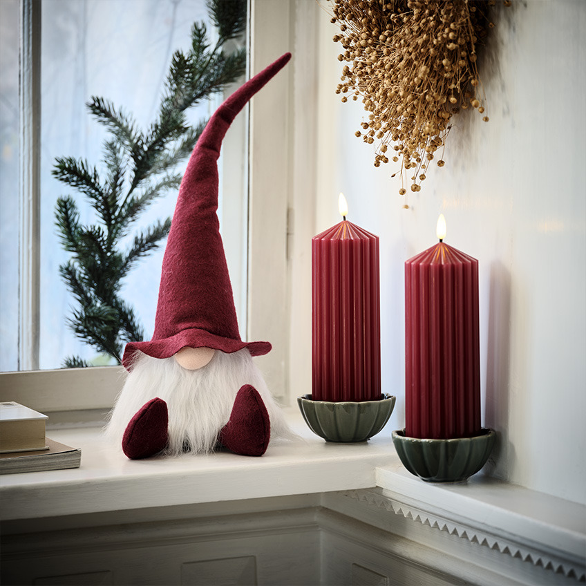 Duende de Natal escandinavo no parapeito da janela junto a grandes velas vermelhas 