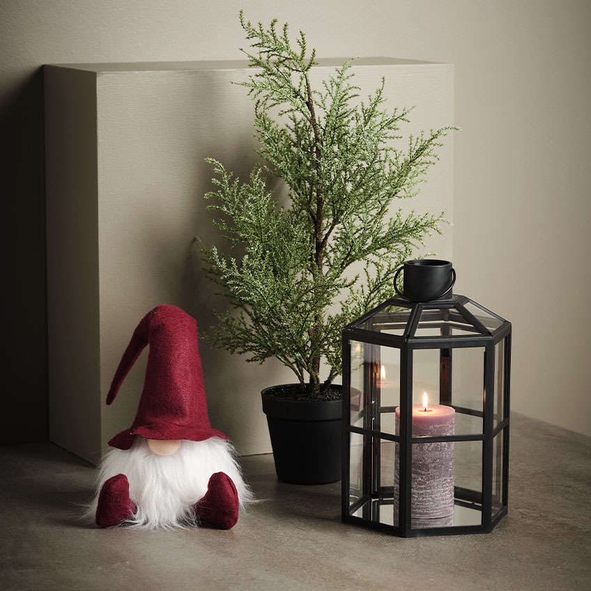 Gnomo de Natal escandinavo ao lado de uma planta artificial e de uma lanterna