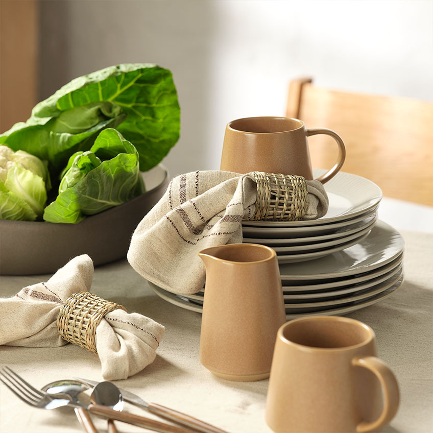 Louça de mesa: Caneca, jarro de leite, guardanapos de pano com argolas para guardanapos e saladeira na mesa de jantar