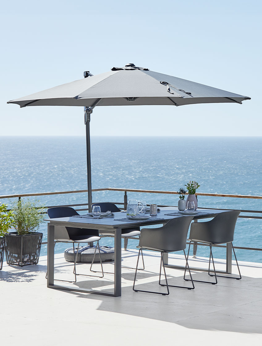 Grande guarda-sol suspenso e mesa e cadeiras de jardim no pátio junto ao oceano