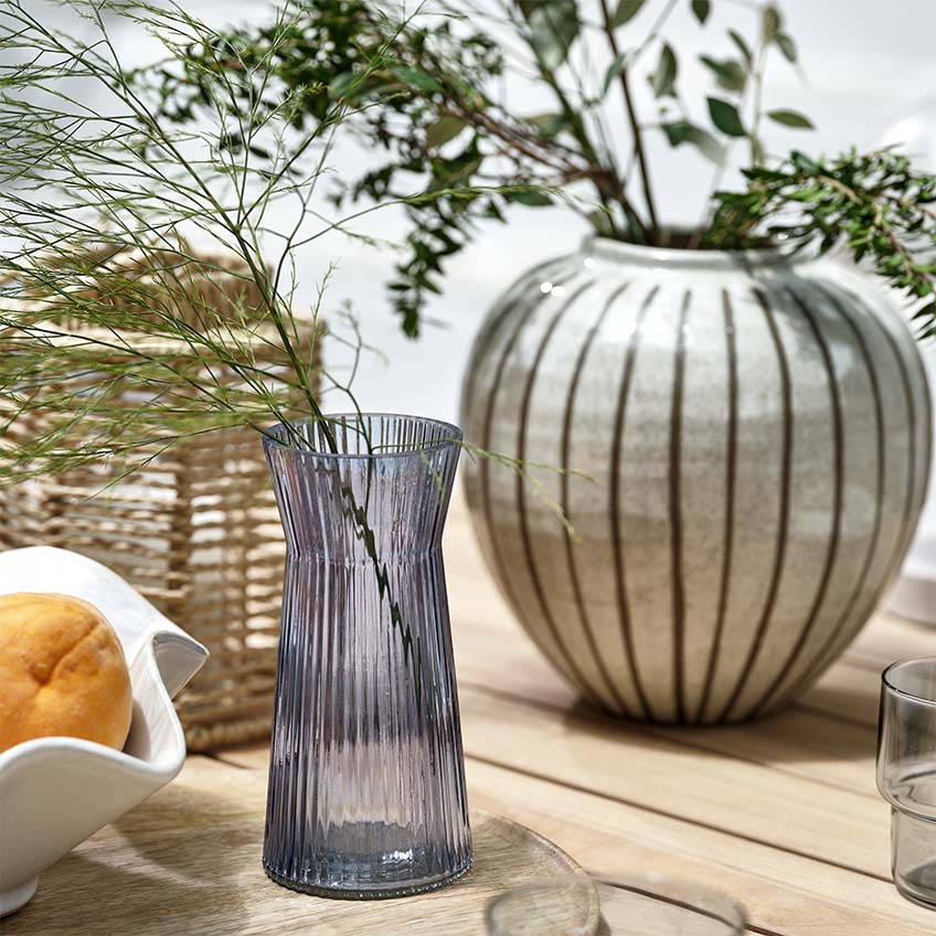 Vasos, lanterna e taça numa mesa de jardim de madeira ao ar livre 