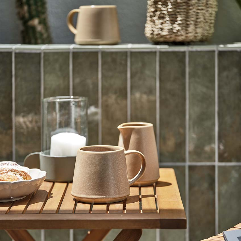 Caneca de café e jarro de leite numa pequena mesa de madeira ao sol 